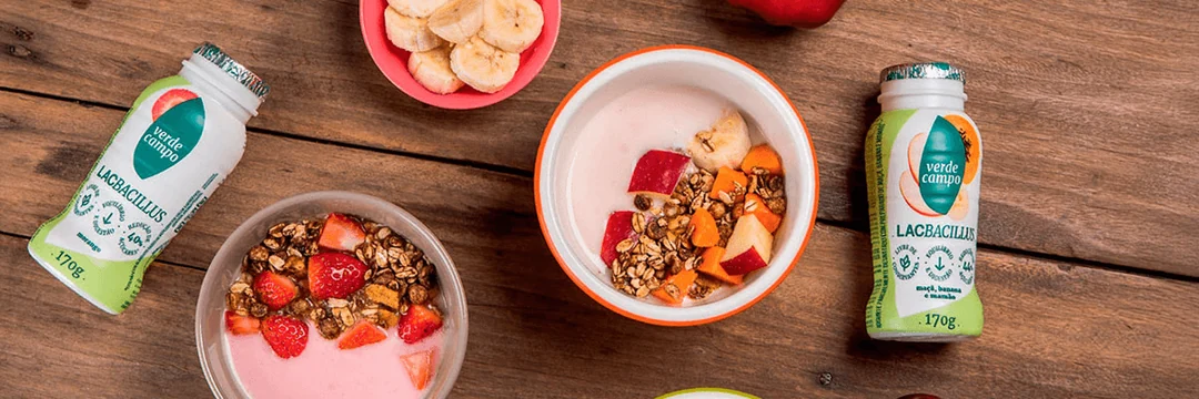 Iogurte com frutas e cereais ao lado de produtos Verde Campo sobre uma mesa